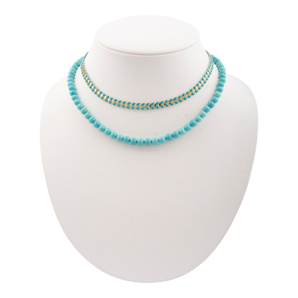 Blue turquoise magnesite layers with golden chevron pendant on a necklace, showcasing vibrant stones and stylish design.