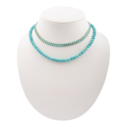 Blue turquoise magnesite layers with golden chevron pendant on a necklace, showcasing vibrant stones and stylish design.