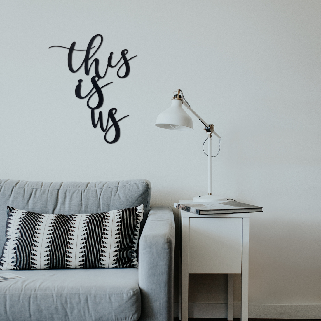 Metal wall art with "This Is Us" design by Malachite, displayed as home decor in a modern living room setting.